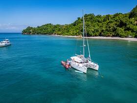 An aerial view of a catamaran anchored near a beautiful beach, with guests enjoying the water and activities — a perfect setting for a tropical getaway.