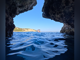 A stunning view from within a rocky cave, showcasing a boat navigating the serene waters along the coastline — a perfect representation of coastal adventures.