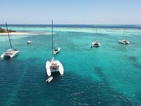 A stunning aerial view of multiple catamarans anchored in crystal-clear turquoise waters, showcasing the beauty of a tropical paradise.
