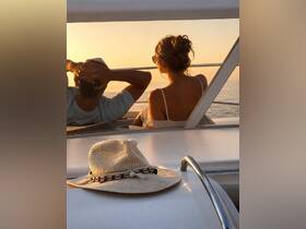 A couple enjoys a serene sunset aboard a yacht, capturing a romantic moment with a stylish hat in the foreground — perfect for intimate getaways on the water.