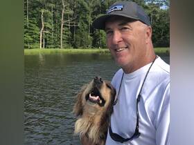 A man enjoys a joyful moment with his dog by the water, showcasing the perfect companionship for a day out on the boat.