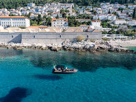 A scenic view of a boat cruising through crystal-clear waters, with a picturesque coastline and charming buildings in the background — perfect for exploring coastal destinations.