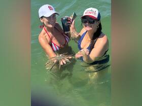 Two women joyfully hold starfish while wading in clear waters, showcasing a fun and interactive wildlife experience.