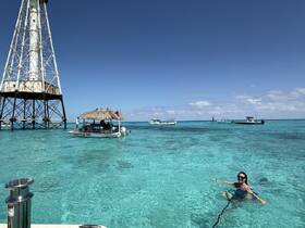 A woman enjoys a refreshing swim in the crystal-clear waters near a boat and a lighthouse, capturing the essence of a perfect beach day.