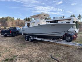A sleek boat named 'FISHON' is showcased on its trailer, parked beside a truck and RV, set against a scenic backdrop of trees and blue skies.