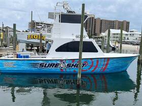 The 'Sure Shot' boat is docked at the marina, showcasing its vibrant design and ready for fishing adventures.