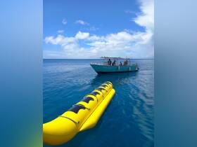 A vibrant yellow banana boat floats in the turquoise waters near the 'Tropic Diver' vessel, perfect for thrilling water activities and fun on the water.