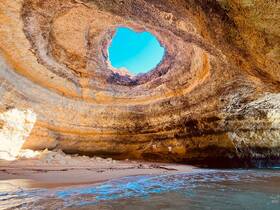 A stunning view of a natural cave with a circular opening, showcasing the beautiful coastline and clear blue sky — a perfect destination for boat tours and exploration.
