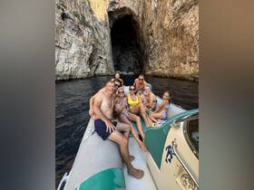 A joyful group of family and friends poses on a boat near a stunning cave, capturing a memorable moment during their aquatic adventure.