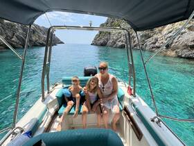 A family enjoys a sunny day on a boat, surrounded by stunning turquoise waters and rocky cliffs — perfect for a memorable day out on the water.