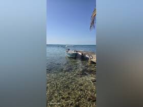 A small boat is docked near a wooden pier, with clear turquoise waters and a serene sky in the background, perfect for a day of exploration.