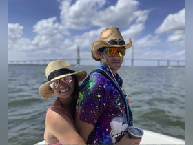 A cheerful couple enjoys their time on a boat with a scenic bridge in the background, perfect for memorable summer adventures on the water.