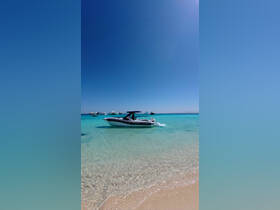 A sleek speedboat glides through the crystal-clear waters near a sandy beach, showcasing the perfect day for boating adventures.