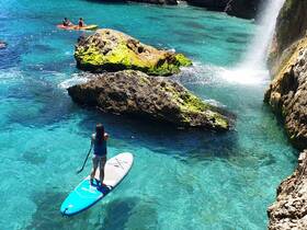 A stunning scene featuring a paddleboarder and kayakers enjoying the crystal-clear waters near a rocky coastline, perfect for adventure seekers and nature lovers.