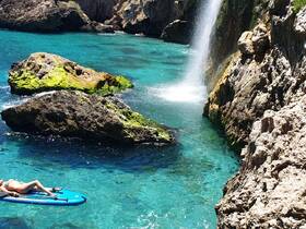 A serene moment of paddleboarding near a stunning waterfall, surrounded by rocky cliffs and crystal-clear waters — a perfect escape for adventure seekers.