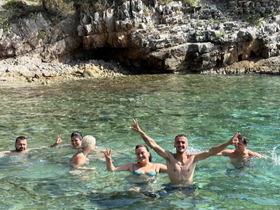 A lively group enjoys a refreshing swim in crystal-clear waters, celebrating their day on the water with smiles and peace signs.