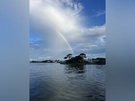 A stunning view of a rainbow arching over tranquil waters, framed by picturesque clouds and waterfront homes — a perfect scene for nature lovers and boaters alike.