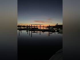 A serene sunset view over a calm marina, showcasing boats docked and their reflections on the water — perfect for peaceful evening escapes.