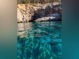 A stunning view of crystal-clear waters revealing underwater rock formations, framed by a rugged coastline — perfect for exploring nature's beauty while boating.