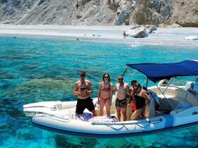 A lively group enjoys a sunny day on a boat in crystal-clear waters, capturing memories against a stunning beach backdrop.