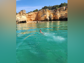 A child joyfully swims in the crystal-clear waters near stunning cliffs, capturing the essence of a perfect beach day.