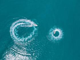 Aerial view of two jet skis creating dynamic water patterns in the turquoise sea, showcasing thrilling on-water activities perfect for adventure seekers.