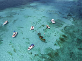 A vibrant aerial view of several boats anchored in crystal-clear waters, with groups of people enjoying snorkeling and swimming — a perfect scene for a fun day on the water.