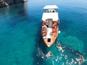 A lively group enjoys a refreshing swim around their boat in crystal-clear waters, perfect for snorkeling and summer fun.