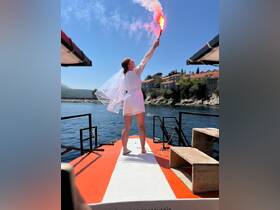A bride joyfully celebrates on the deck of a boat, holding a flare against a stunning backdrop, capturing the essence of a memorable wedding experience on the water.