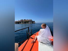 A bride enjoys a serene moment on a boat, overlooking a picturesque coastal landscape — a perfect backdrop for wedding celebrations.
