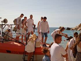 A lively group dressed in white disembarks from a boat onto a beautiful beach, creating a festive atmosphere perfect for celebrations or weddings.