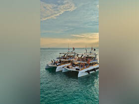 A lively group enjoys a sunset cruise aboard two catamarans, perfect for celebrations and fun on the water.