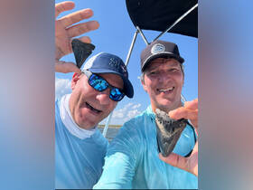 Two friends proudly display their shark teeth finds while enjoying a day out on the water — a perfect adventure for fossil hunting enthusiasts.
