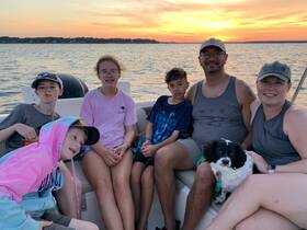 A joyful family enjoys a sunset boat ride, capturing a perfect moment with their dog on board — ideal for family outings and memorable experiences on the water.