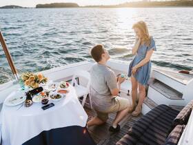 A romantic proposal takes place on a boat at sunset, complete with a beautifully set table and a stunning backdrop — perfect for unforgettable moments on the water.