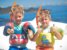 Two excited children give thumbs up while wearing snorkeling gear and floaties, ready for a fun day of water activities.