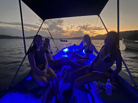 A group of friends enjoys a vibrant sunset on a boat, illuminated by blue lights, creating a perfect atmosphere for a memorable evening on the water.