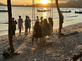 A lively group enjoys a sunset moment on the beach, capturing memories while swinging and celebrating together — perfect for group outings and beach parties.