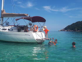 A joyful family enjoys a sunny day on the water, with children swimming and playing around a sailboat, creating unforgettable memories in a beautiful tropical setting.