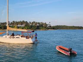 A group enjoys a sailing experience on a beautiful day, with a tropical island backdrop and a dinghy nearby, perfect for exploring the serene waters.