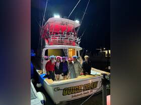 A lively group poses on the fishing boat 'Quick Draw' at night, wearing colorful hats and celebrating their time on the water — perfect for memorable fishing adventures.