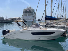 A sleek sport deck boat docked in a marina, showcasing its modern design against a backdrop of other vessels and a cruise ship.