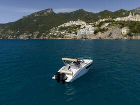 A stunning aerial view of a sleek speedboat cruising through vibrant blue waters, with picturesque coastal scenery in the background — perfect for exploring the Amalfi Coast.