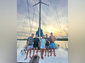 A cheerful group poses on the deck of a sailboat during sunset, capturing the joy of their sailing adventure.