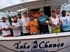 A group of fishermen celebrates their successful catch aboard the 'Take a Chance' boat in Barbados, showcasing camaraderie and the thrill of fishing adventures.