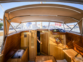 The interior of a beautifully crafted boat helm, showcasing wooden finishes and navigational equipment, with a person visible in the cabin area.