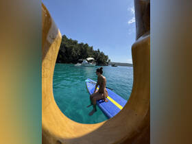 A woman enjoys paddleboarding in crystal-clear waters, with a boat anchored nearby, creating a perfect scene for summer adventures and relaxation.