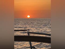 A stunning sunset over the ocean, framed by the railing of a boat, creating a serene atmosphere perfect for evening cruises.