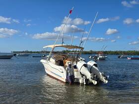 A fisherman stands beside a boat in shallow water, surrounded by other vessels, showcasing a perfect day for fishing and exploration.