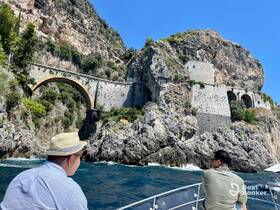 Two guests enjoy a scenic boat ride along the stunning coastline, featuring a historic bridge and rocky cliffs — a perfect backdrop for exploration and adventure.